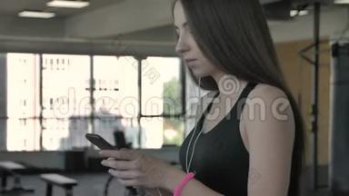 美丽的运动女孩听智能手机音乐，应用程序在跑步机上运行